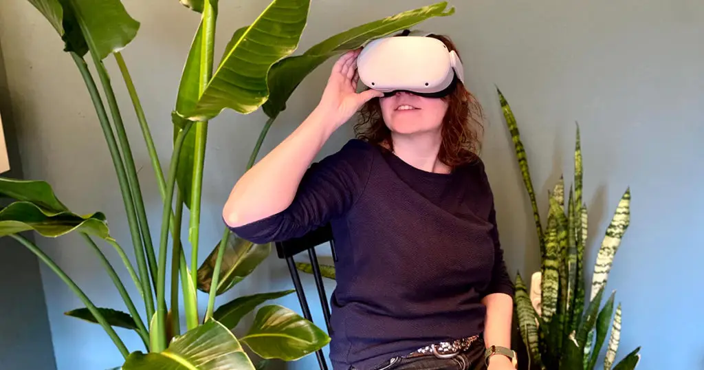Eine Frau sitzt mit einer VR-Brille auf dem Kopf umgeben von Pflanzen. Es geht um das Thema virtuelles Reisen. 