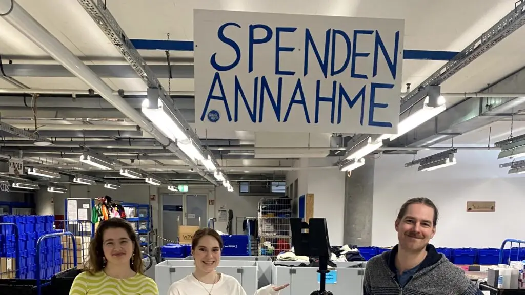 Drei Personen vor der Spendenannahme von Hanseatic Help mit Kamera auf Stativ