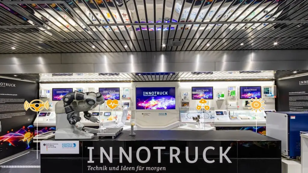 Ausstellungsbereich im InnoTruck mit Roboterarm, Exponaten und Infopunkten im virtuellen Rundgang